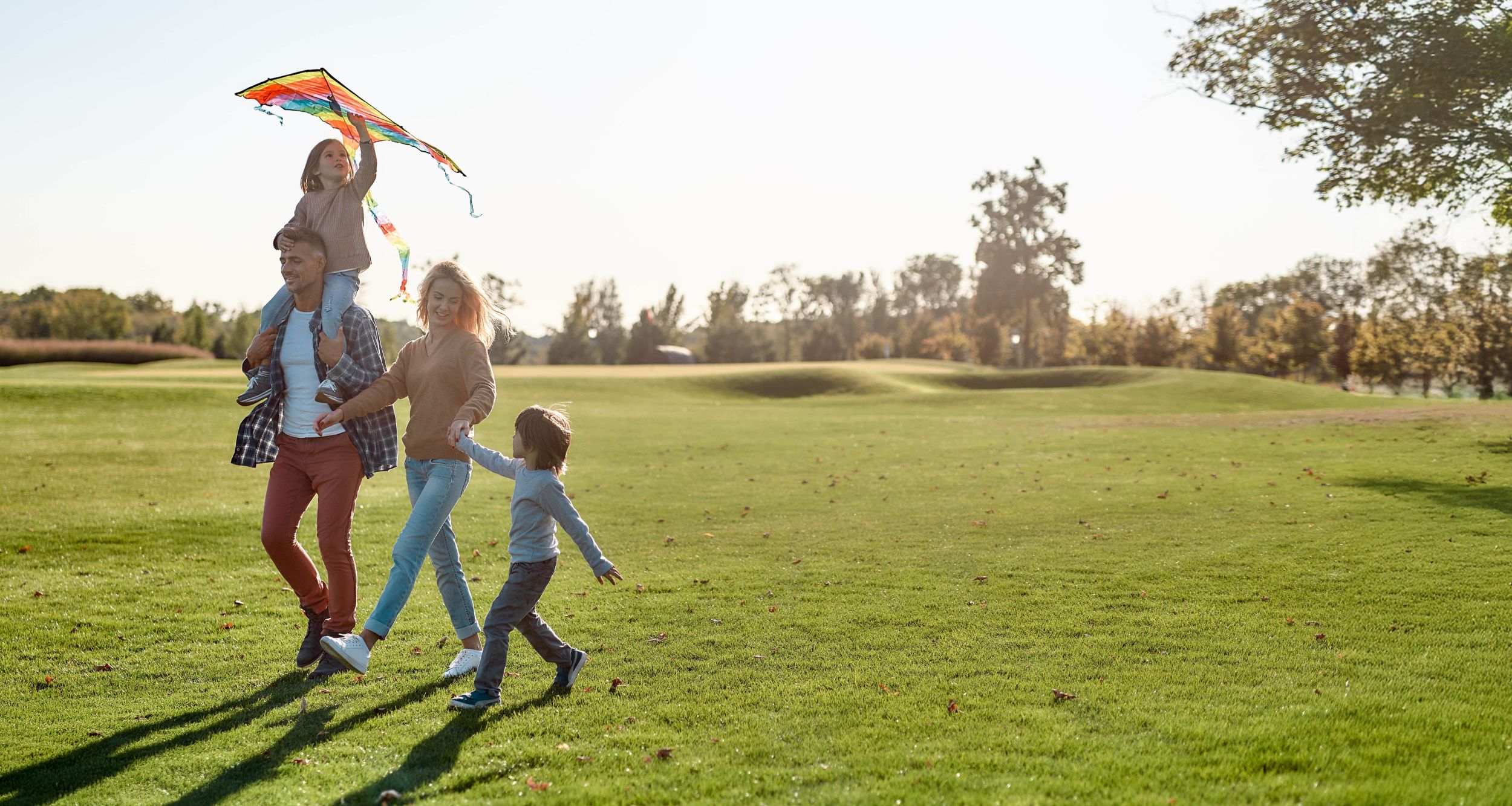 Eltern und zwei Kinder spazieren glücklich durch den Park mit einem Flugdrachen.