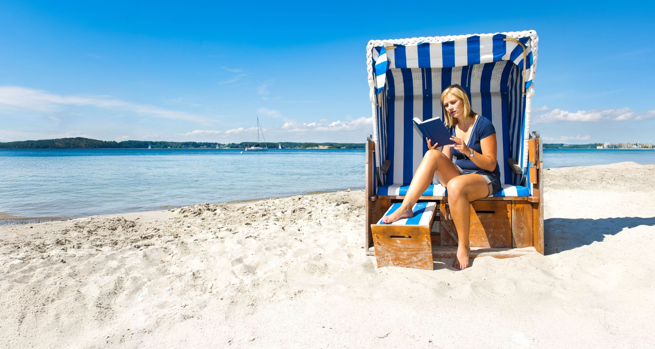 Eine Frau liest ein Buch am Sandstrand in einem Strandkorb.
