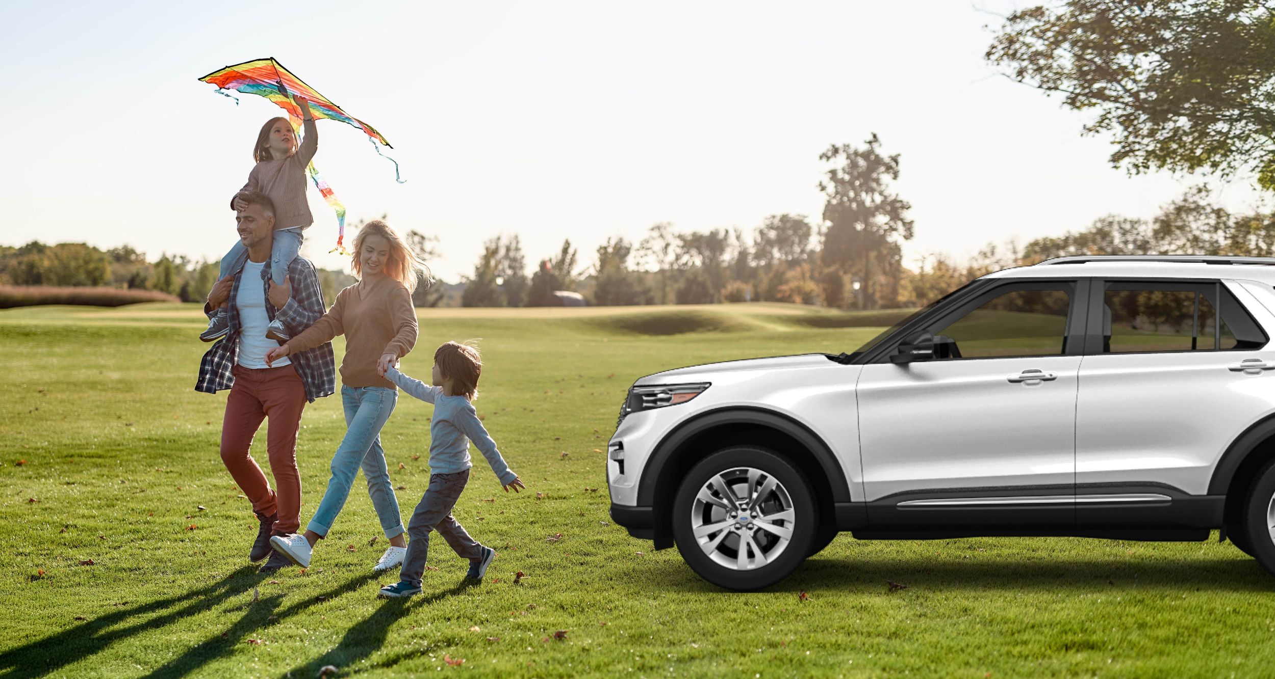 Eltern und zwei Kinder spazieren glücklich durch den Park mit einem Flugdrachen.