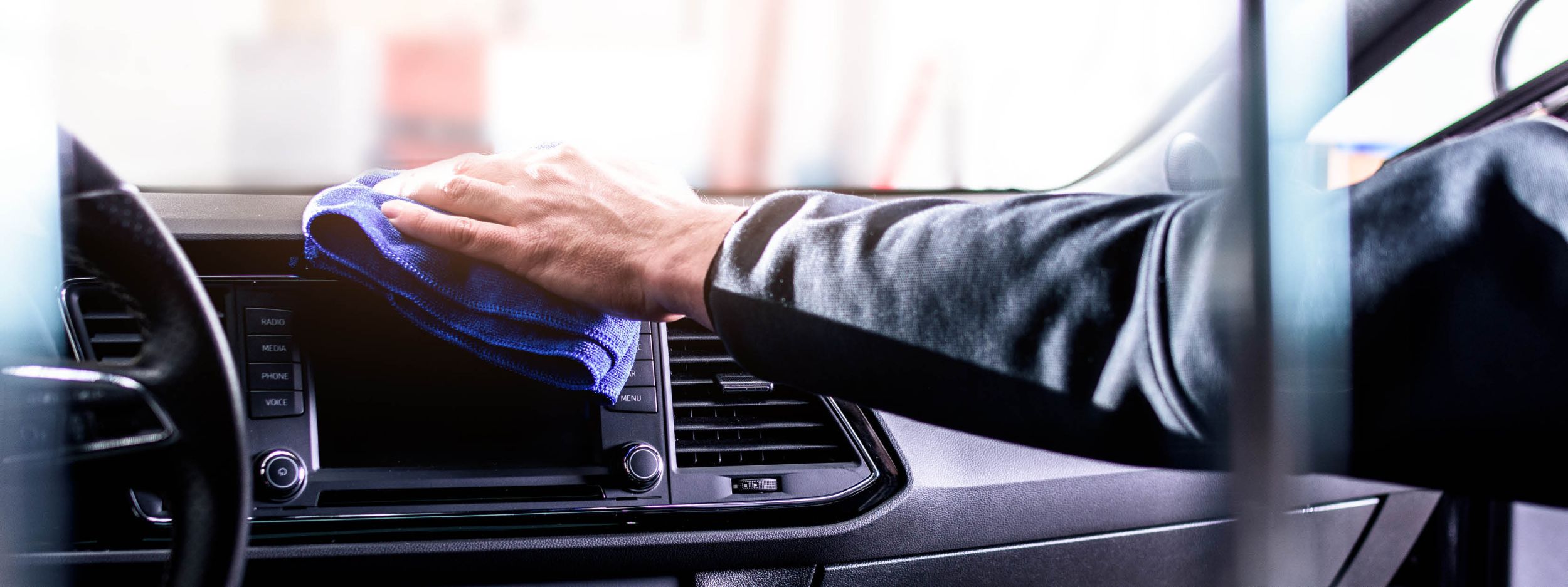 Ausgestreckte Hände mit dem blauen Lappen putzen die Autoarmatur.