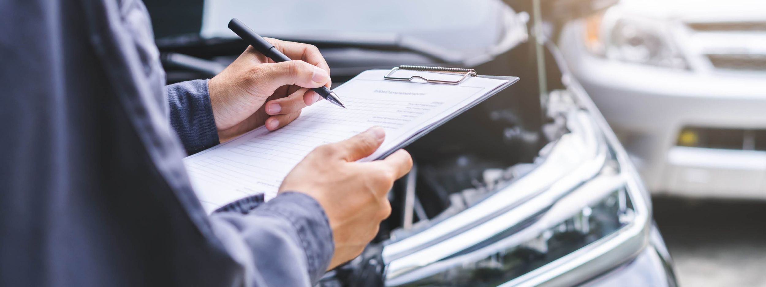 In den Händen wird ein Checkblock gehalten vor einer offenen Autohaube